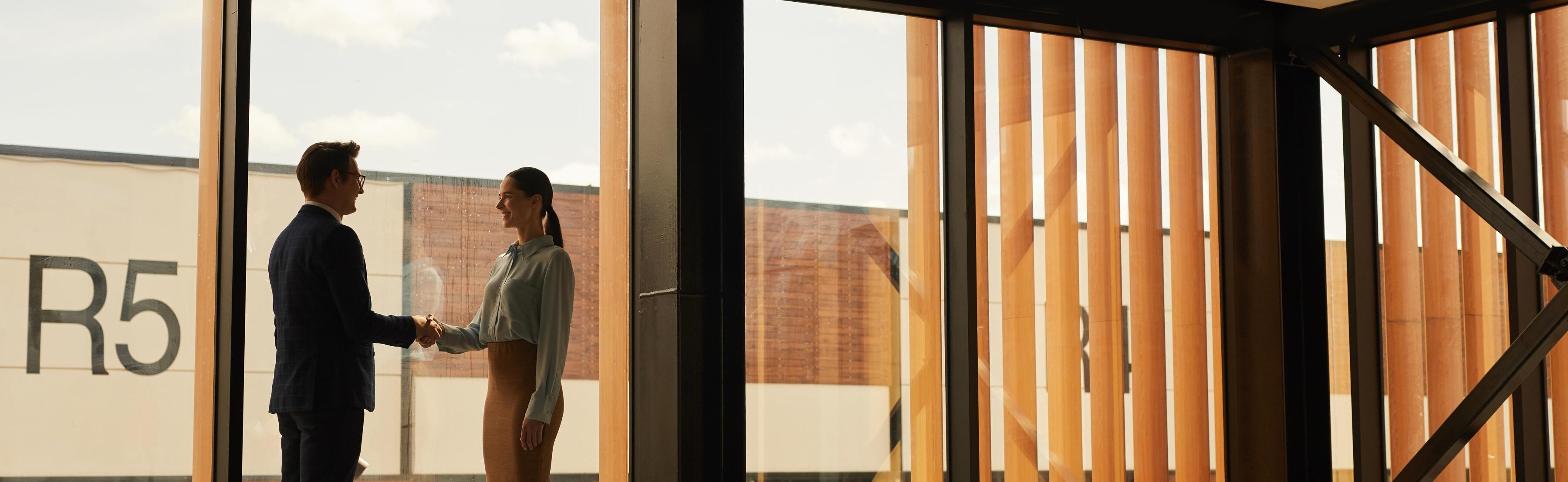 Wide angle view of a real estate agent shaking hands with a client while standing in an empty office building