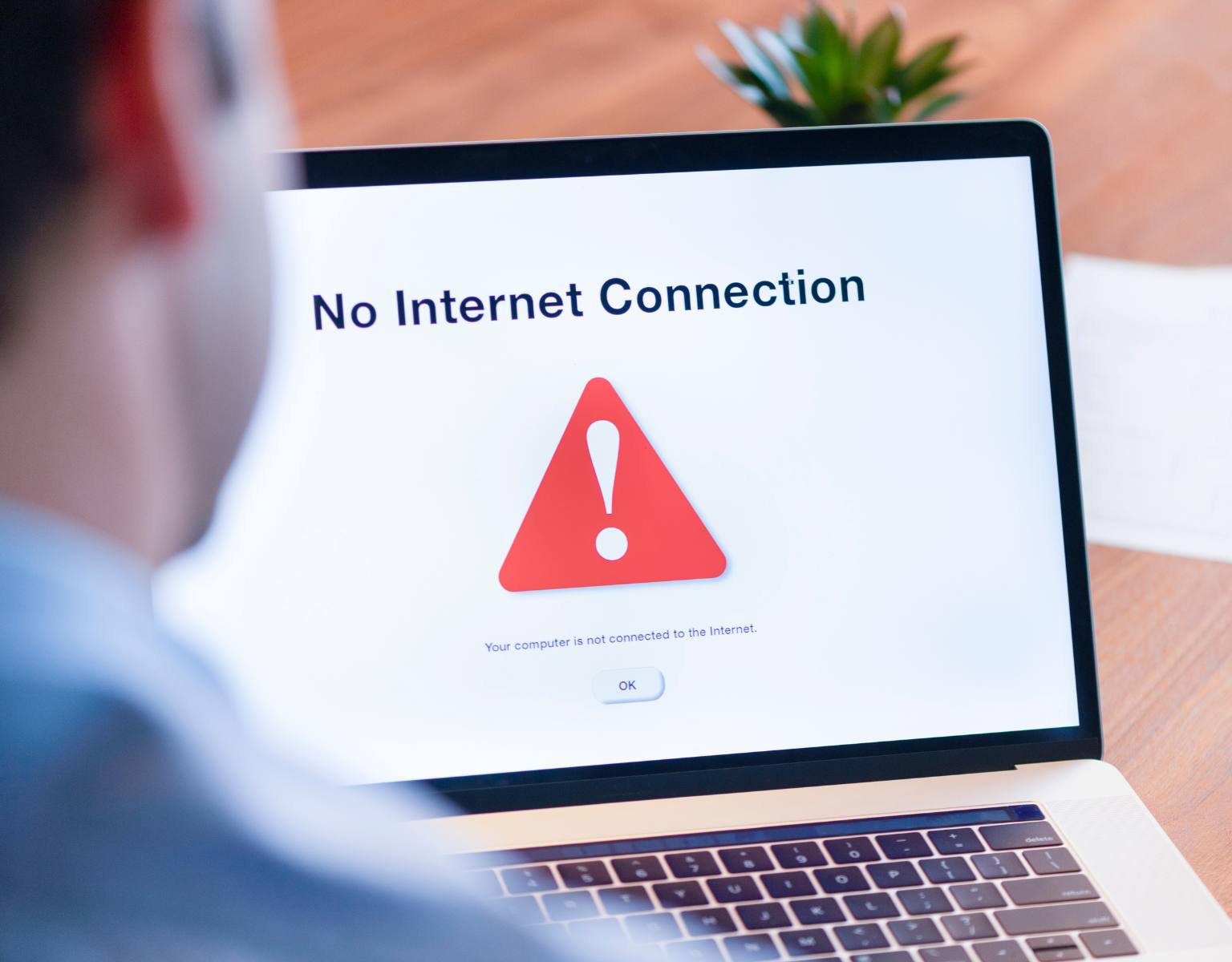 Business man with his back to the camera and slightly out of shot looks at a computer screen with the words, "No Internet Connection" and a warning symbol