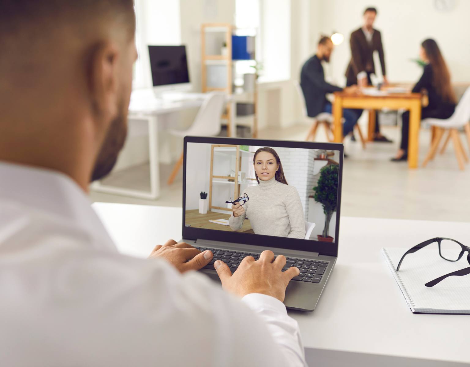 A man with his back to the camera holds a video conference with a woman via a laptop computer